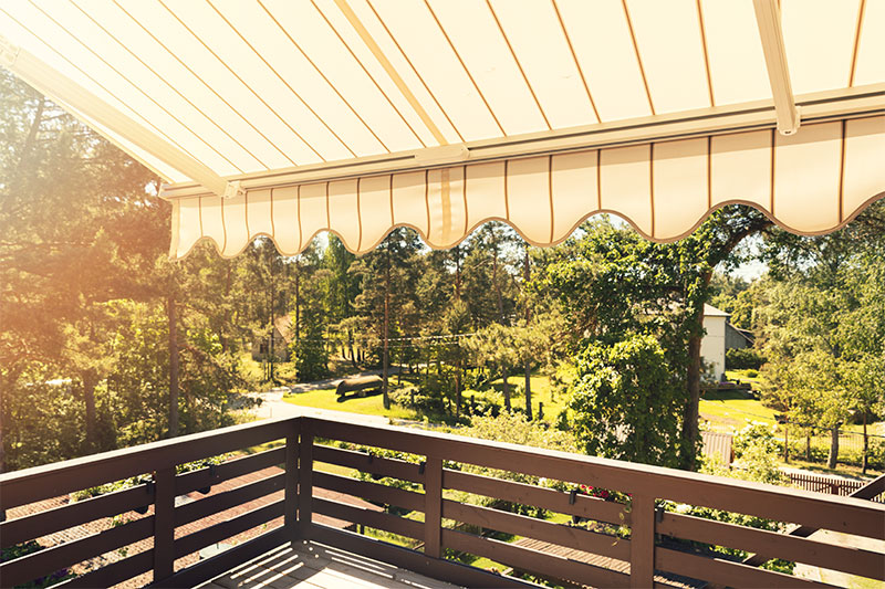Bild Markise Bild einer Markise über einem großen Balkon mit Blick zu einem Garten bei Sonnenschein